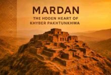A modern aerial view of Mardan city showing busy roads, buildings, greenery, and mountains, representing the Hidden Heart of Khyber Pakhtunkhwa.