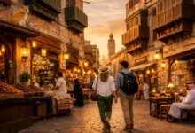 First-time travelers walking through Al-Balad, Jeddah at sunset with historic coral-stone buildings, rawasheen balconies, and market stalls.