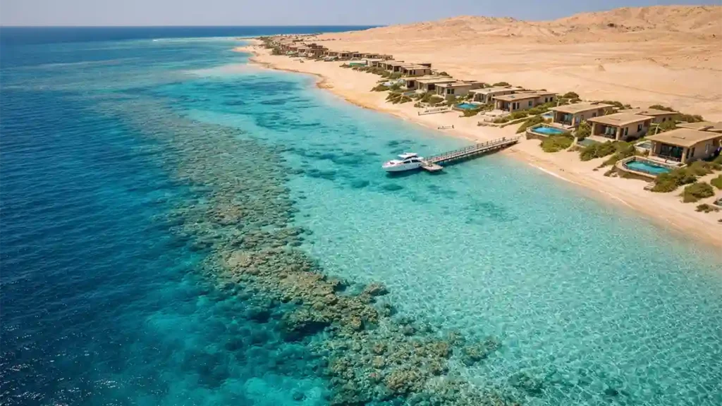 Aerial view of turquoise Red Sea water, coral reef edge, and a modern eco-resort villas along Saudi Arabia’s coastline