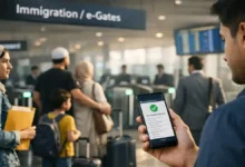 Traveler holding a phone with e-immigration verification screen near Pakistan airport immigration e-gates as other passengers queue.