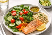 Balanced plate method meal with half vegetables, grilled salmon, quinoa, and a small serving of avocado on a white plate.