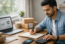 Young Pakistani entrepreneur planning a low-investment business at a home office with laptop, budget notes, calculator, and parcels.