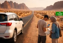 Two travelers check a map beside a white SUV on a desert highway in Saudi Arabia at golden hour, with rock formations in the background.
